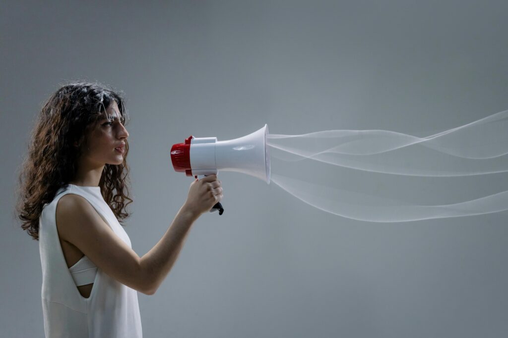 Join Us in Transforming Research Impact Woman using a megaphone emitting sound waves on a gray background.